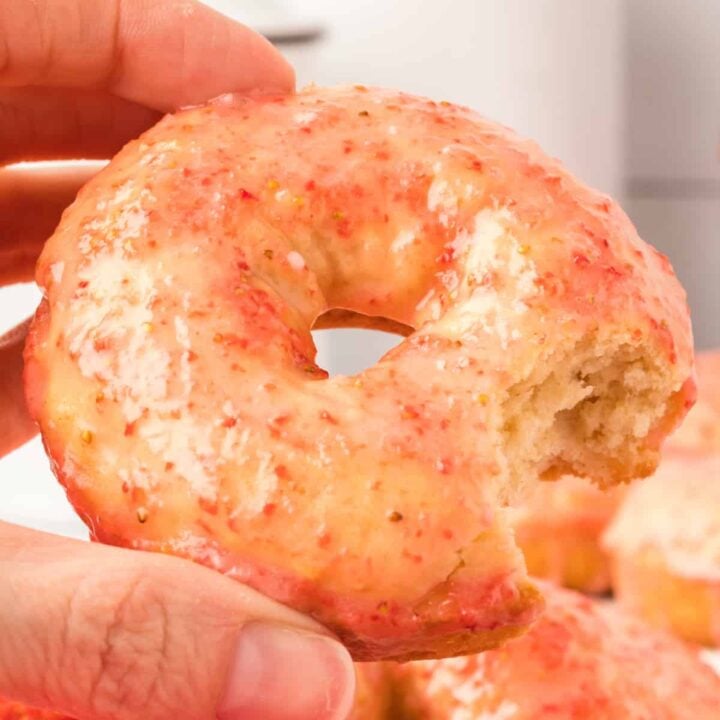 hand holding a vanilla cake donut with strawberry galze