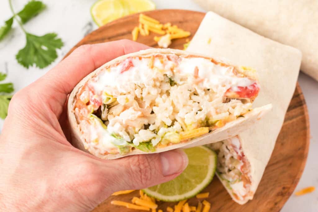hand holding a cut burrito showing layers of beans, rice, cheese, sour cream, and vegetables