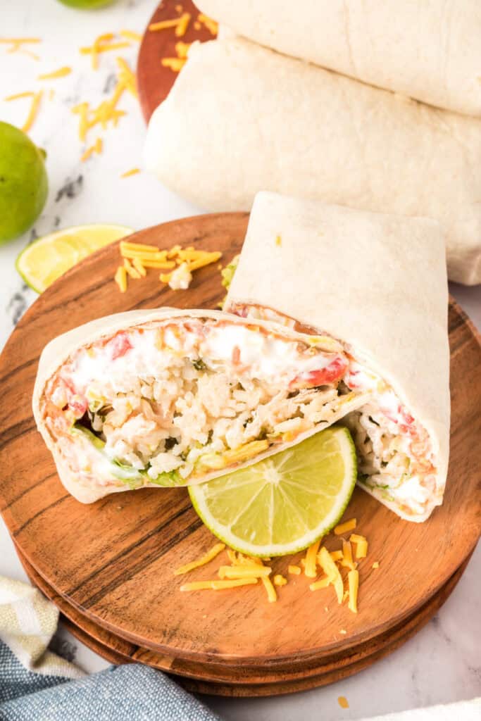cut burrito halves on a wooden board with a lime slice and shredded cheese scattered around