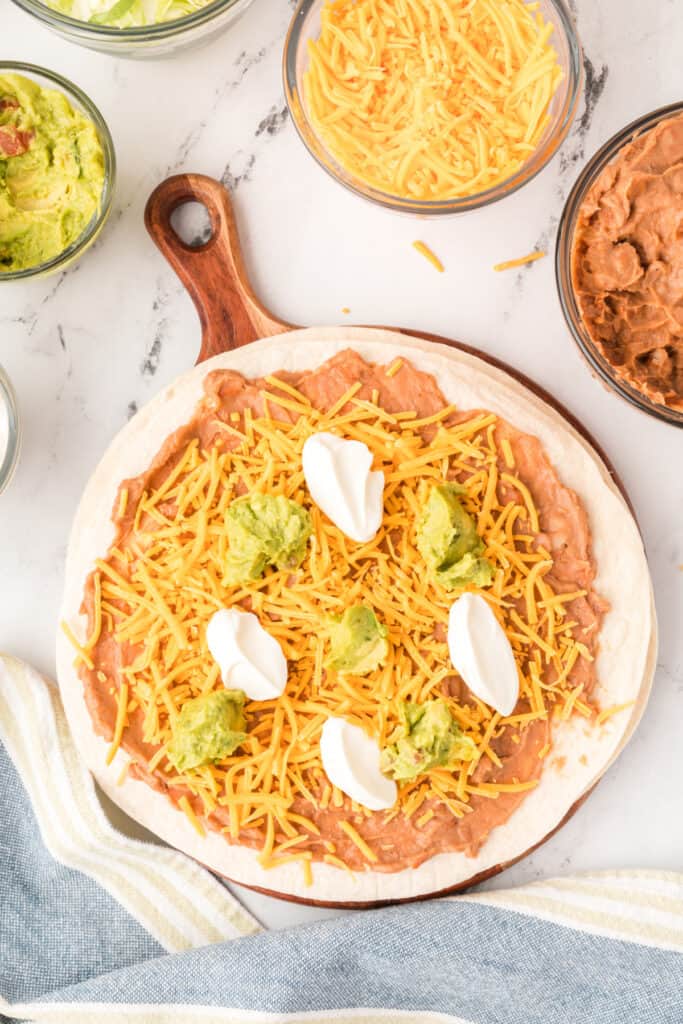 tortilla with refried beans and cheese topped with dollops of sour cream and guacamole
