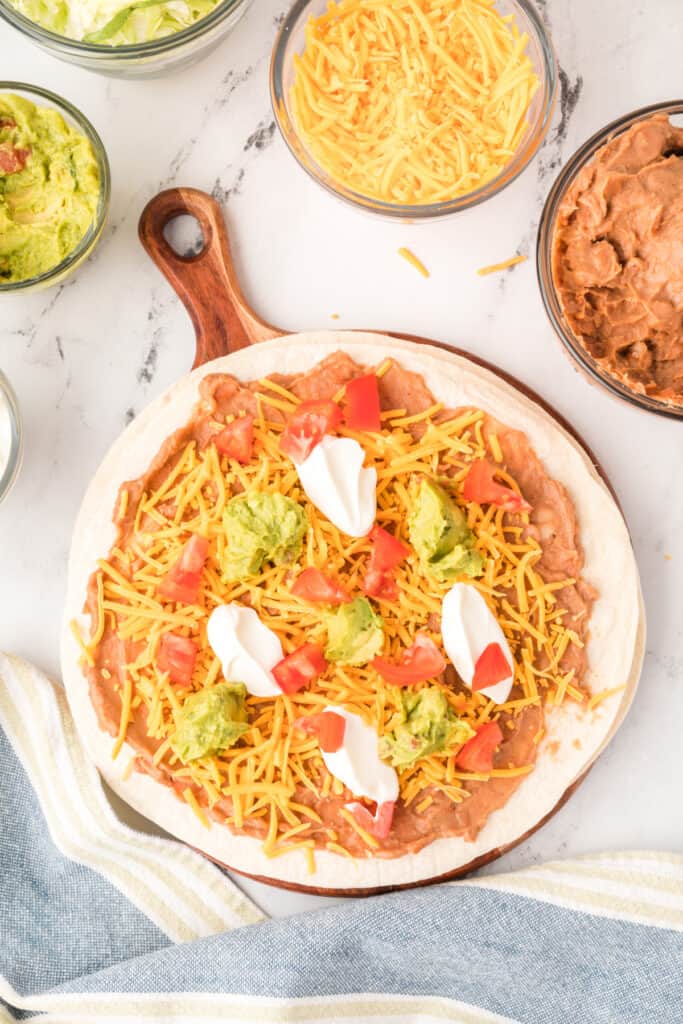 tortilla with beans, cheese, sour cream, and guacamole topped with chopped tomatoes
