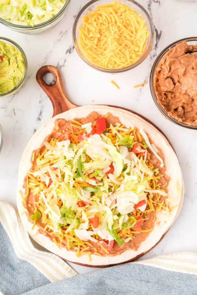 tortilla layered with beans, cheese, sour cream, guacamole, tomatoes, and shredded lettuce
