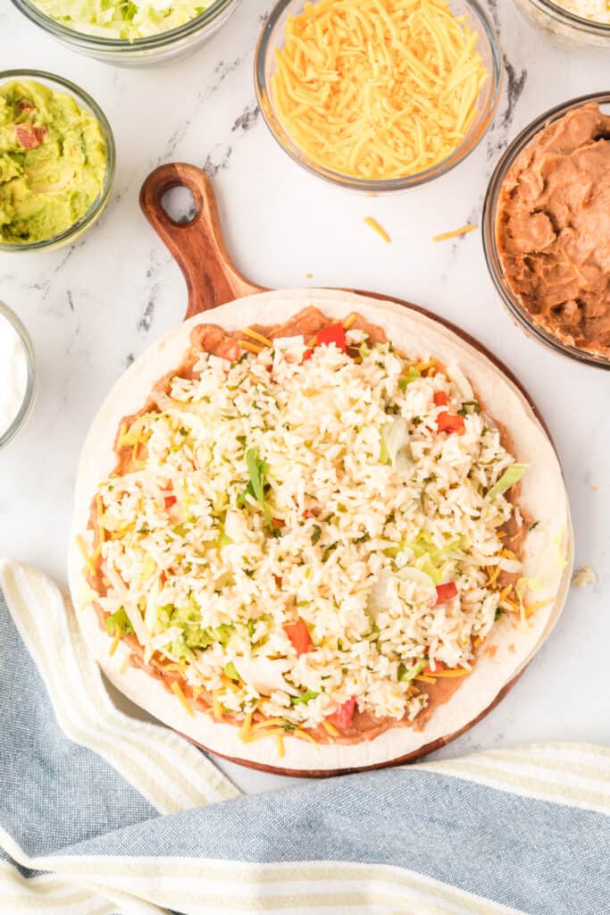 tortilla layered with beans, cheese, sour cream, guacamole, tomatoes, lettuce, and cilantro lime rice