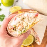 hand holding a cut burrito showing rice, beans, sour cream, cheese, and vegetables with a lime slice in the background