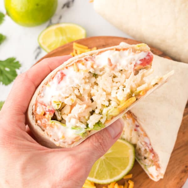 hand holding a cut burrito showing rice, beans, sour cream, cheese, and vegetables with a lime slice in the background