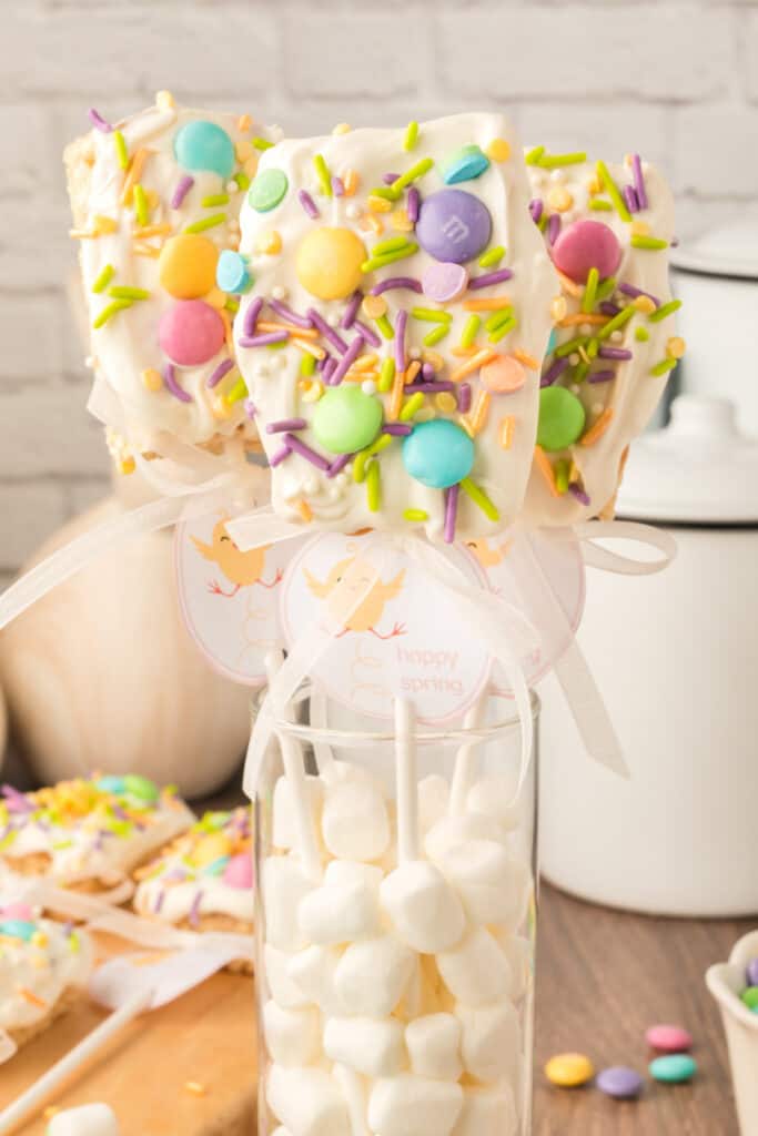 three spring rice krispies treats pops in glass cylinder filled with mini marshmallows
