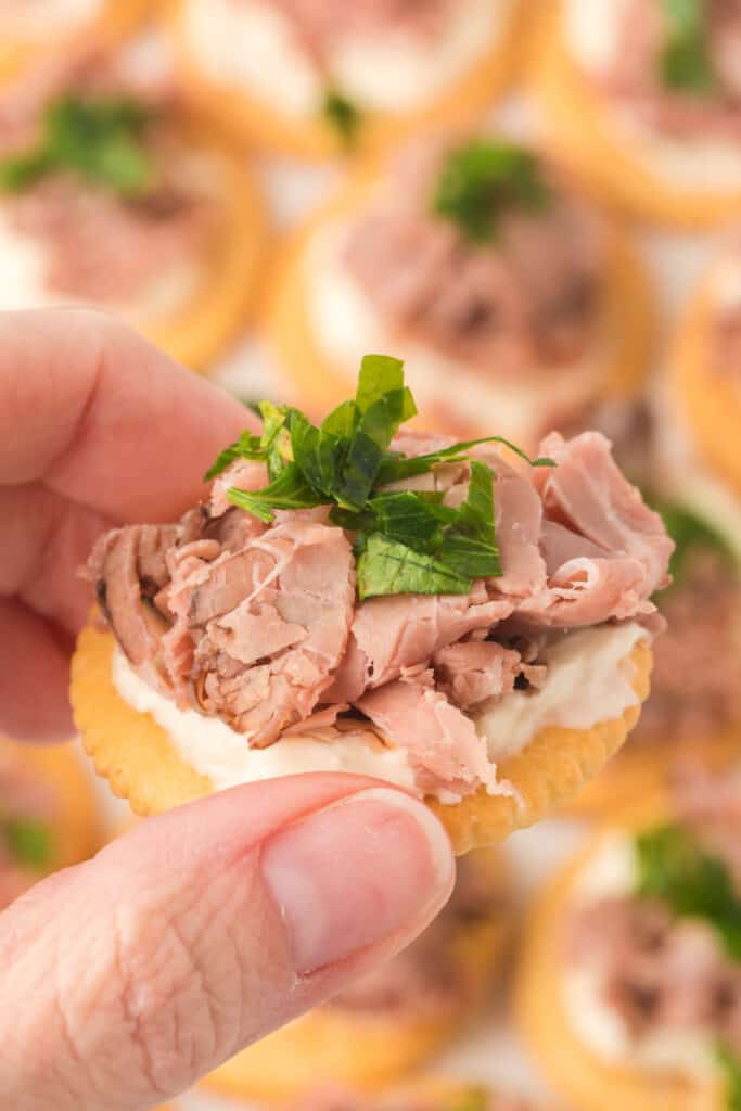 closeup of a hand holding a roast beef horseradish cream cheese snack cracker