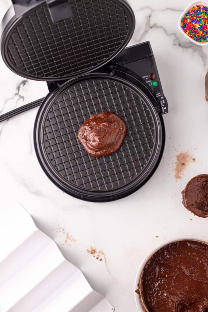 Chocolate batter added to a waffle cone maker to cook homemade chocolate taco shells.