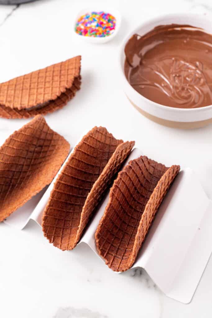 Homemade chocolate taco shells cooling in a taco holder before filling with ice cream.