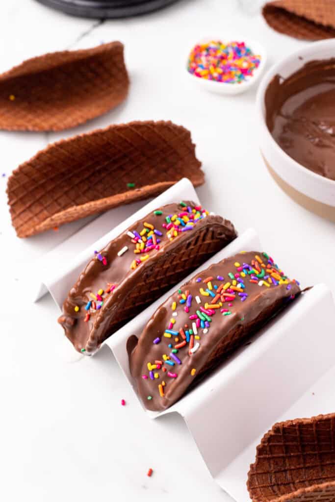 Homemade Choco-Tacos coated in chocolate and topped with rainbow sprinkles before freezing.