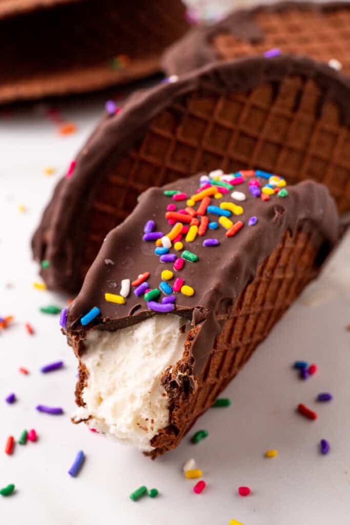 Bite taken from a homemade Choco-Taco showing creamy vanilla ice cream inside a chocolate waffle shell.