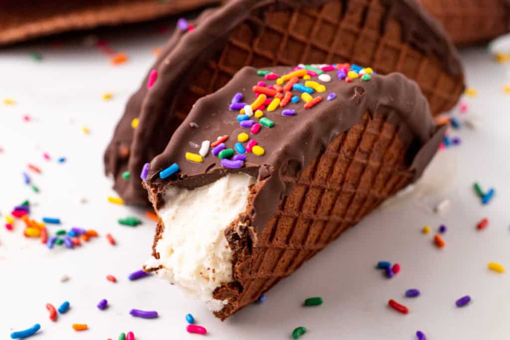 Close-up of a bitten homemade Choco-Taco with vanilla ice cream, chocolate coating, and rainbow sprinkles.