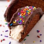 Homemade Choco-Taco with a bite missing, featuring vanilla ice cream, chocolate coating, and rainbow sprinkles.