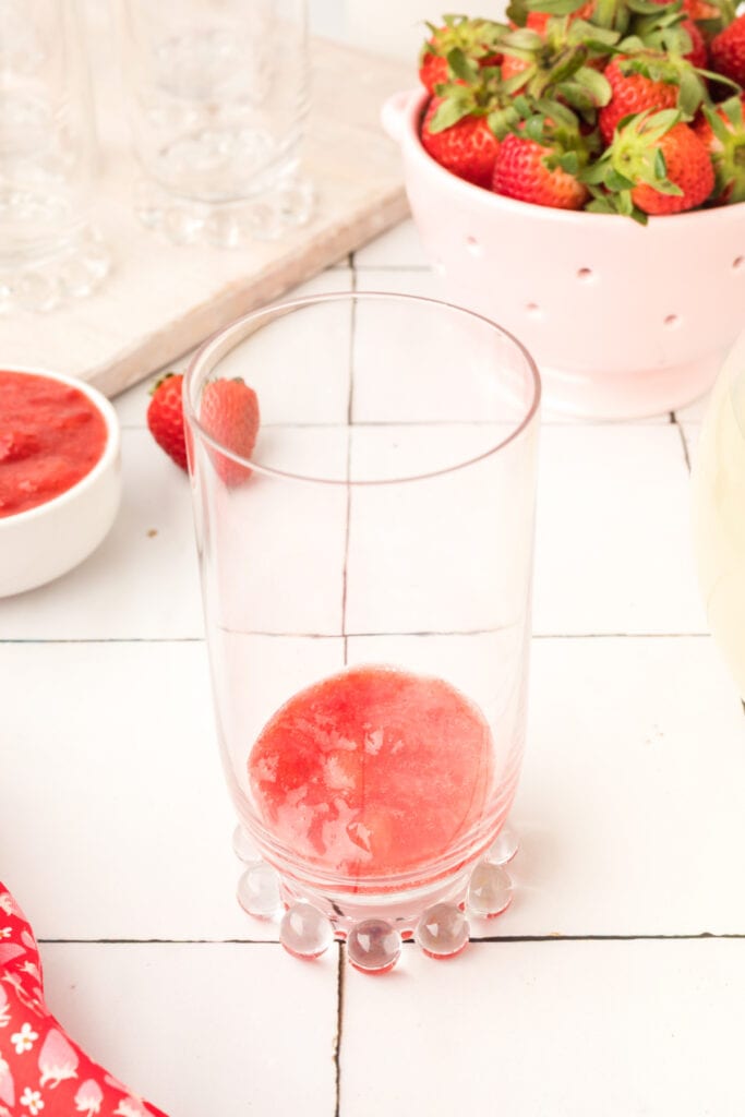 Strawberry topping spooned into the bottom of a serving glass before adding ice.