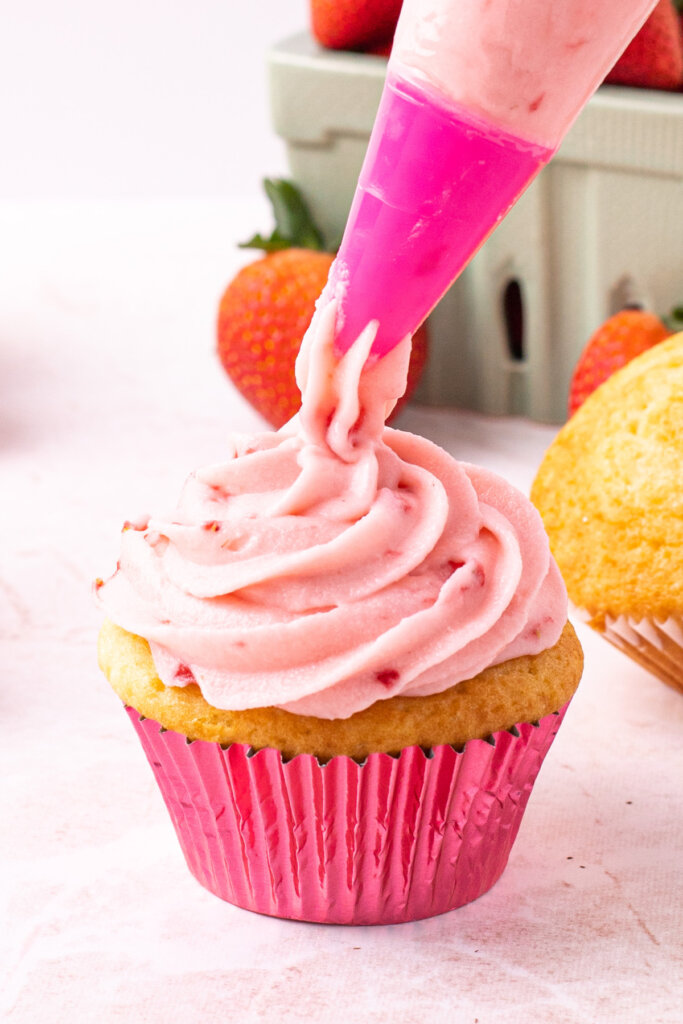 strawberry buttercream being piped onto a cupcake