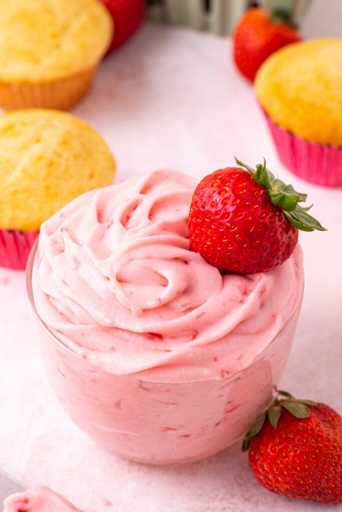 glass jar filled with strawberry buttercream frosting topped with a strawberry