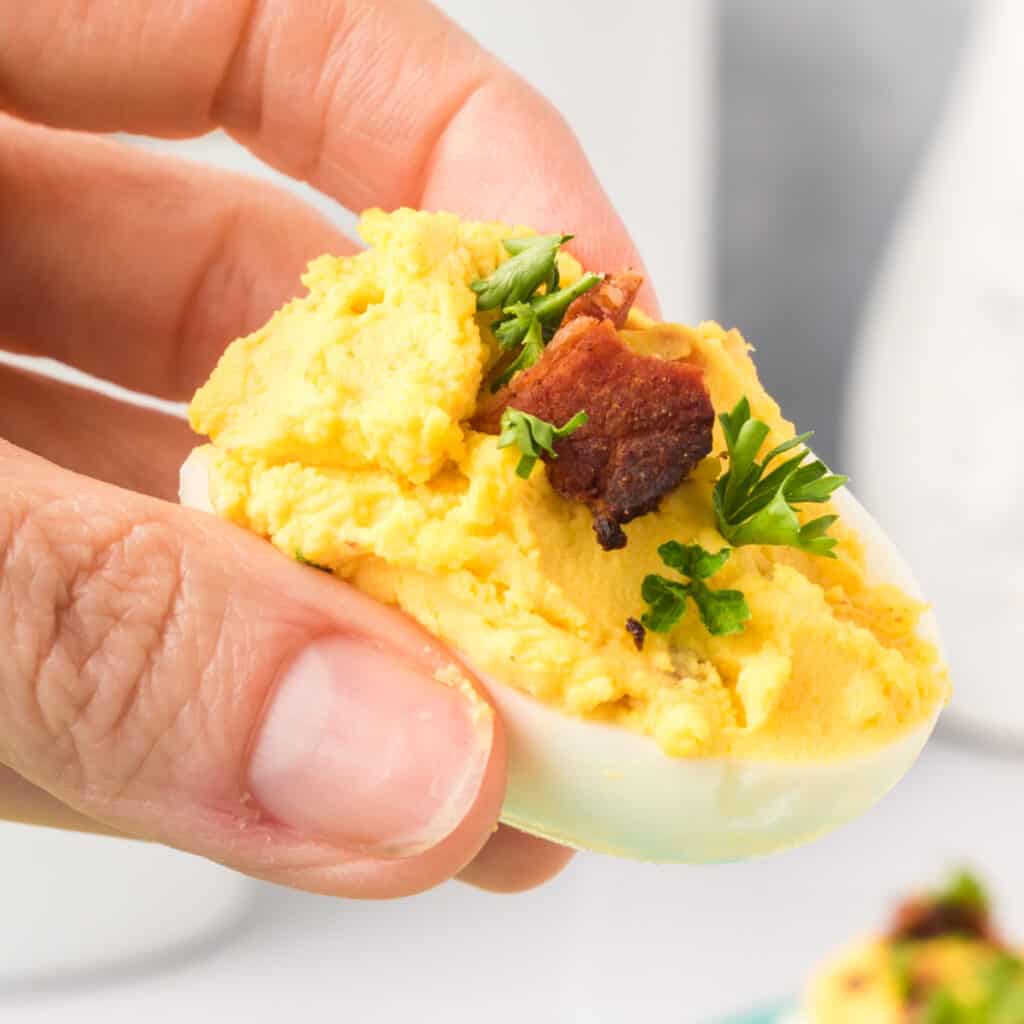 closeup of hand holding bacon cheddar deviled egg