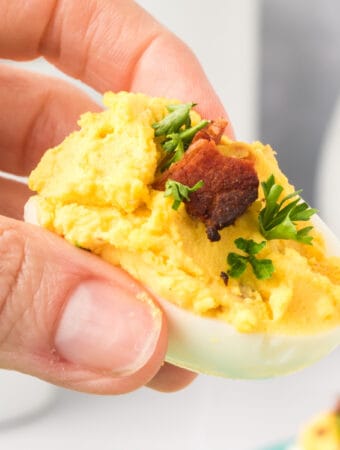 closeup of hand holding bacon cheddar deviled egg