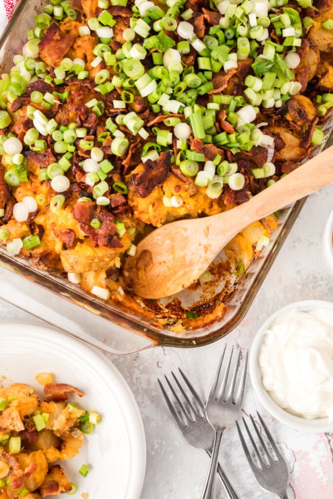 loaded potato and chicken casserole in baking dish with spoon in spot with scoop taken out