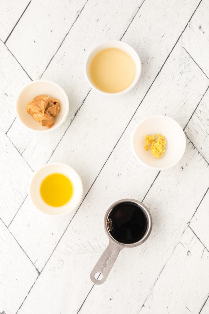 small bowls with soy sauce, peanut butter, oil, rice vinegar, and grated ginger on a white wood surface