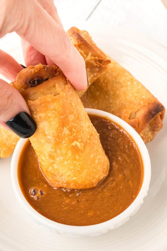 hand dipping egg roll into thai peanut sauce