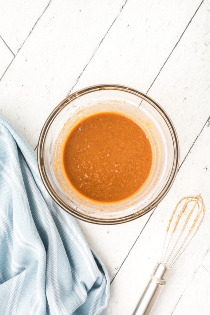 glass bowl with mixed thai peanut sauce and whisk on white surface