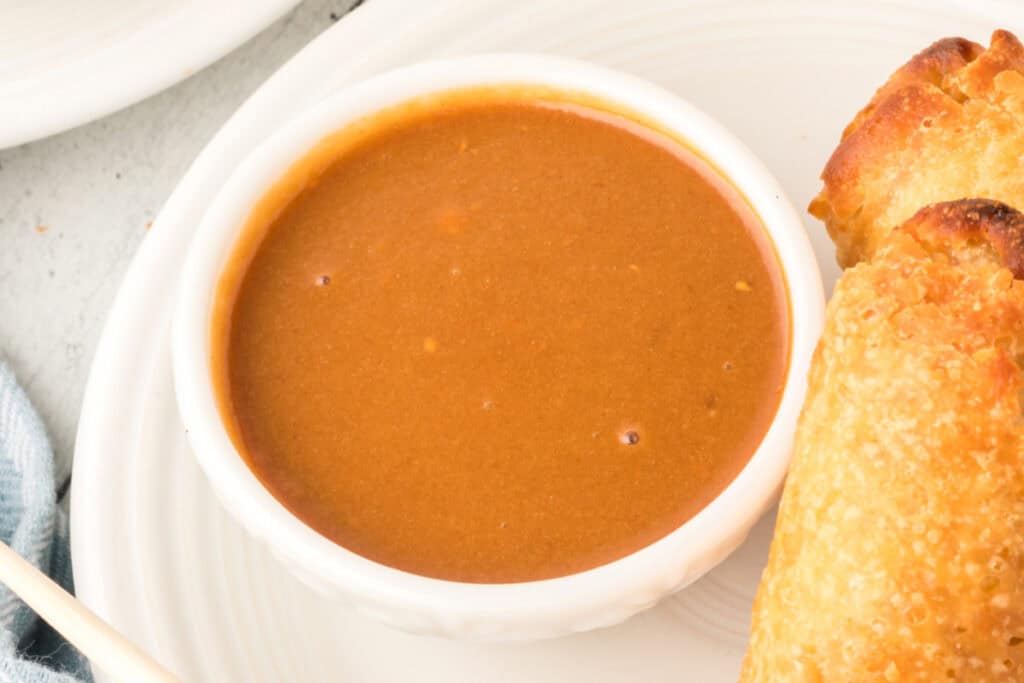 thai peanut sauce in bowl served with egg rolls on a plate