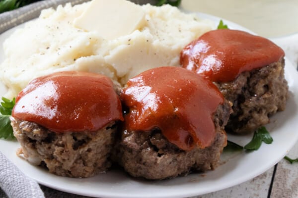 three meatloaf muffins on plate with mashed potatoes