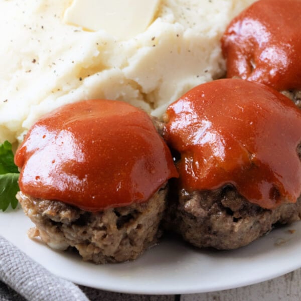three meatloaf muffins lined up on a plate with mashed potatoes