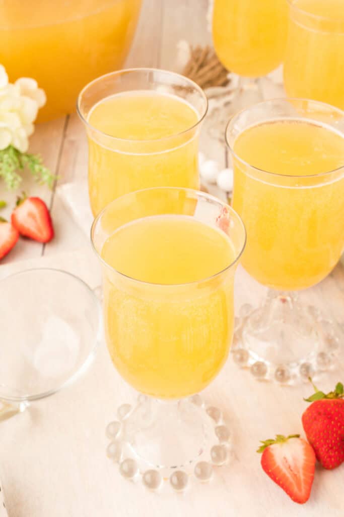 Close-up of glasses filled with bubbly mock champagne punch garnished with strawberries and surrounded by fruit.