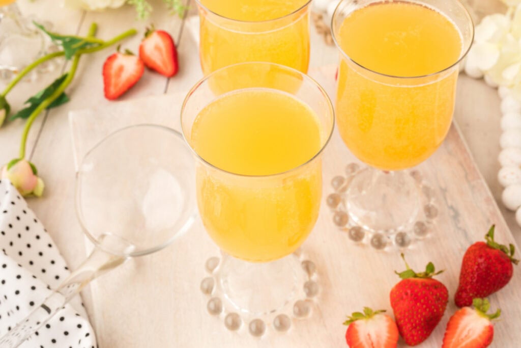 Overhead shot of three glasses of mock champagne punch with strawberries and flowers arranged around the serving area.