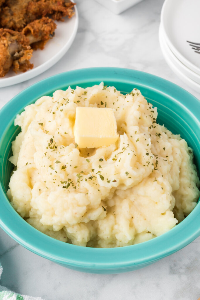 fluffy mashed potatoes topped with butter in an aqua colored bowl