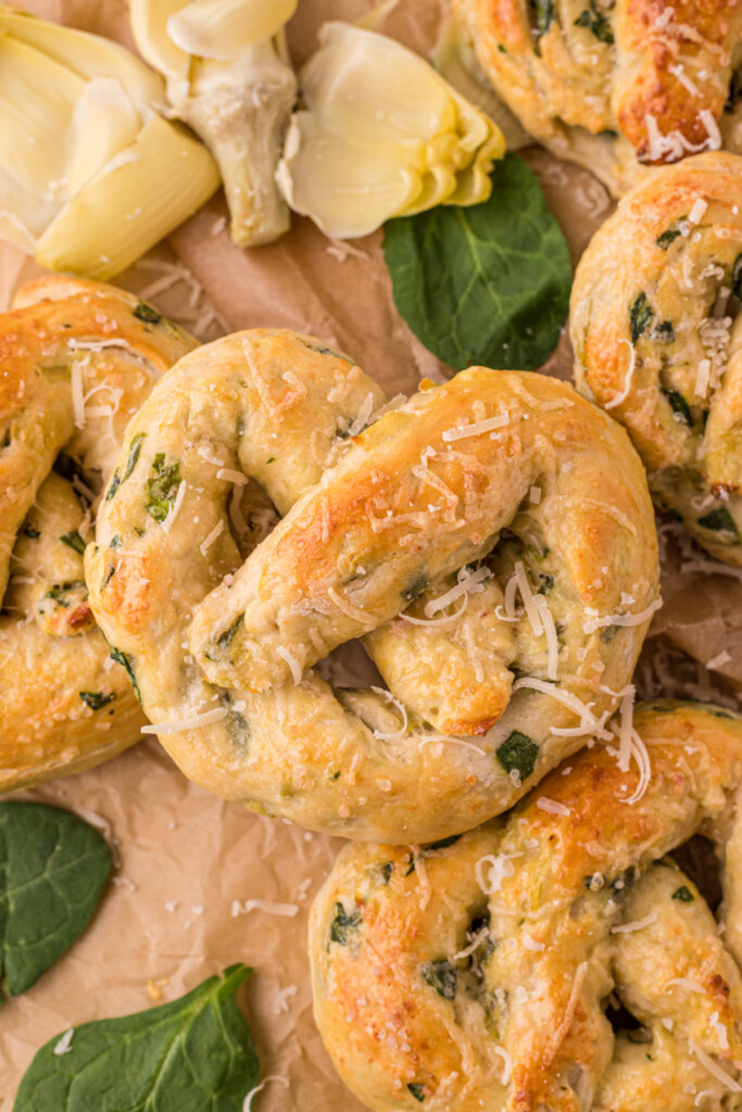 spinach artichoke pretzels on brown paper with artichokes and spinach