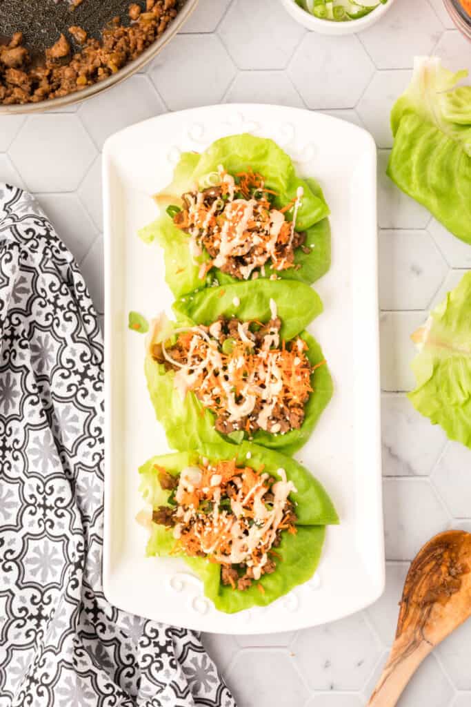 Asian Pork Lettuce Wraps topped with shredded carrots, green onions, sesame seeds, and Sriracha ranch drizzle