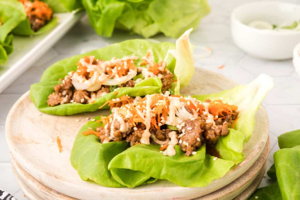 plated Asian Pork Lettuce Wraps on a wooden board with sauce drizzle and toppings