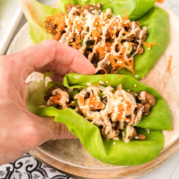 hand holding an Asian Pork Lettuce Wrap in butter lettuce with ground pork, shredded carrots, sesame seeds, and Sriracha ranch drizzle
