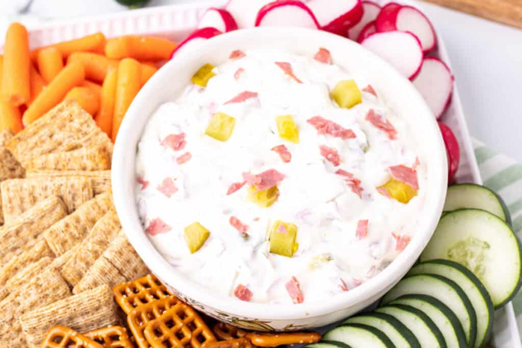 Close-up of finished dip served in a bowl surrounded by crackers, pretzels, and veggies