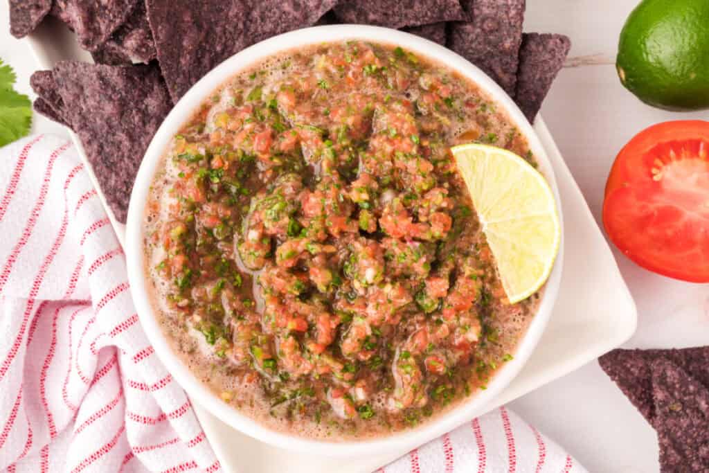 Bowl of fresh homemade salsa garnished with a lime wedge, served with blue corn tortilla chips
