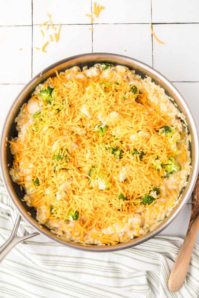 Shredded cheddar cheese melted over Cheesy Chicken Broccoli Rice Skillet in a large skillet with broccoli, chicken, and rice