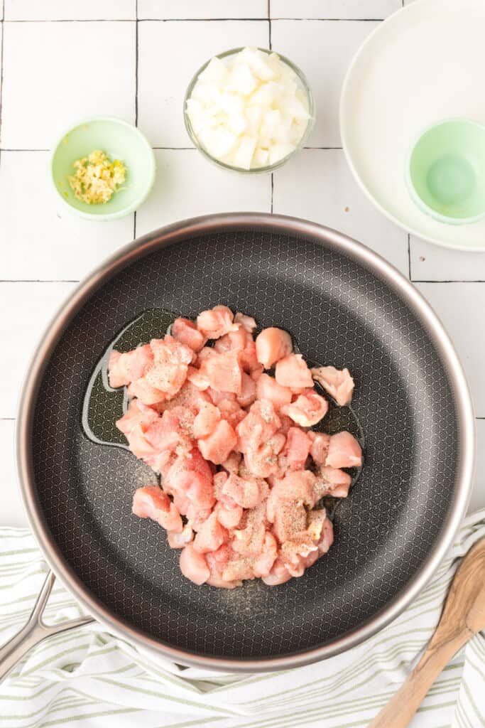 Bite-sized chicken pieces cooking in a large skillet with oil, salt, and pepper for Cheesy Chicken Broccoli Rice Skillet