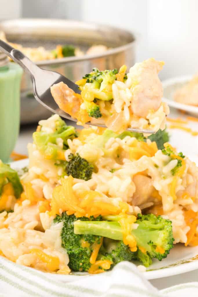 Close-up of Cheesy Chicken Broccoli Rice Skillet with broccoli, chicken, creamy rice, and melted cheddar cheese on a fork