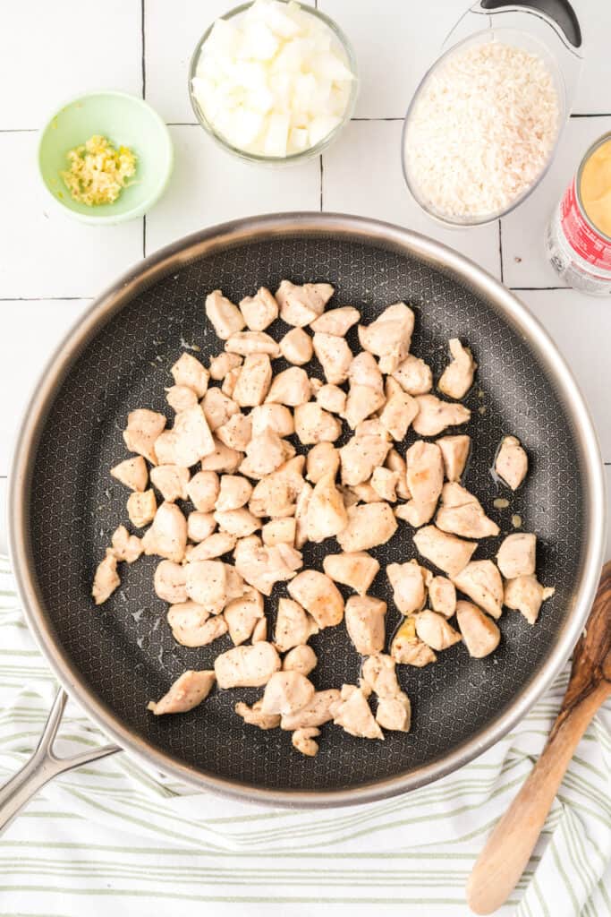 Cooked chicken pieces in a skillet for Cheesy Chicken Broccoli Rice Skillet with rice, onion, garlic, and cream of chicken soup nearby