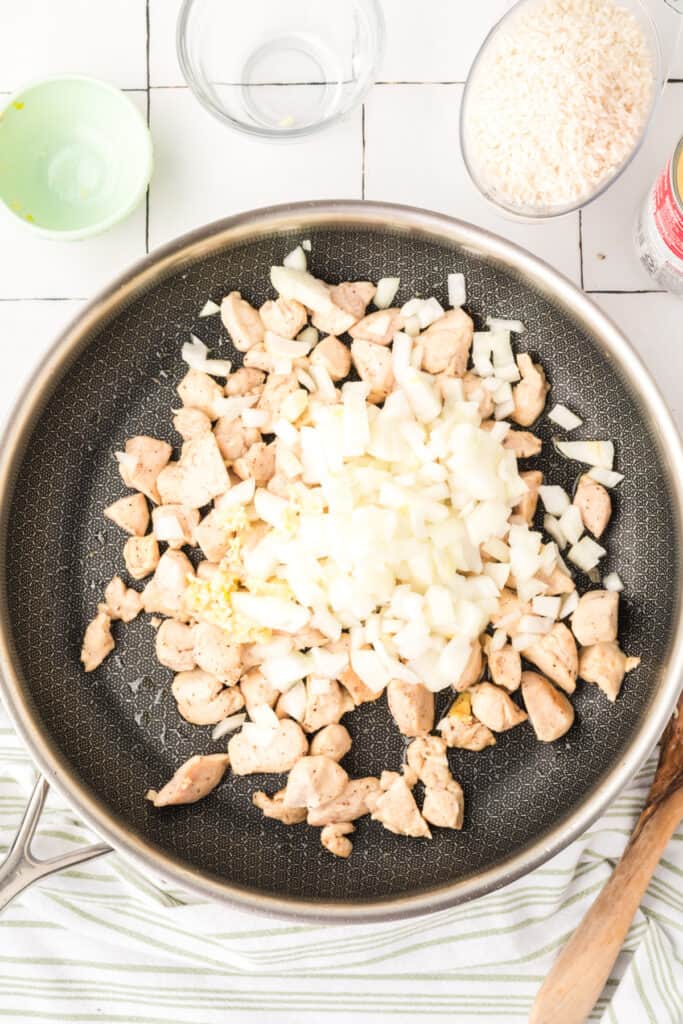 Diced onion and garlic added to cooked chicken in a skillet for Cheesy Chicken Broccoli Rice Skillet