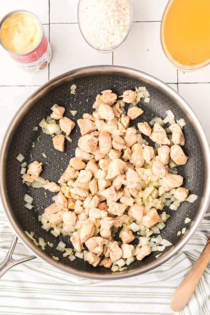 Chicken and onion mixture cooking in a skillet for Cheesy Chicken Broccoli Rice Skillet with rice, broth, and cream soup nearby