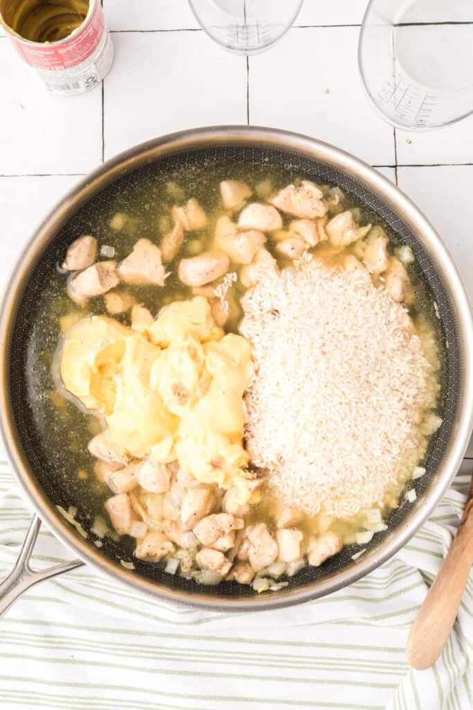 Rice, broth, and cream of chicken soup added to chicken in a skillet for Cheesy Chicken Broccoli Rice Skillet