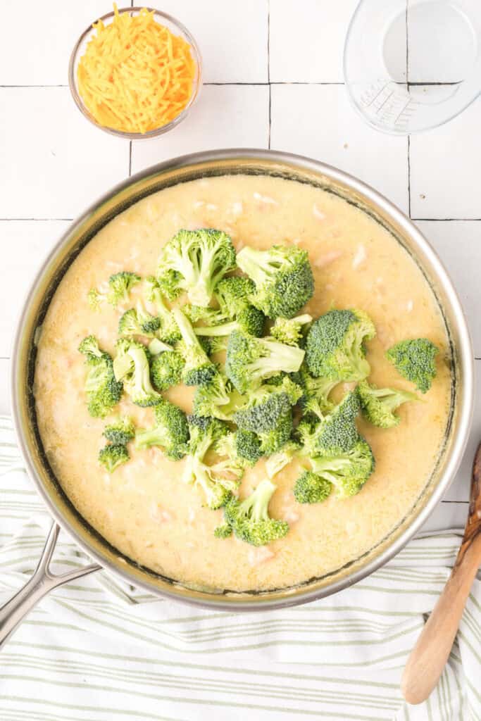 Fresh broccoli added to creamy chicken and rice mixture in a skillet for Cheesy Chicken Broccoli Rice Skillet