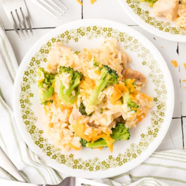 Square image of Cheesy Chicken Broccoli Rice Skillet served on a plate with broccoli, chicken, rice, and melted cheddar cheese