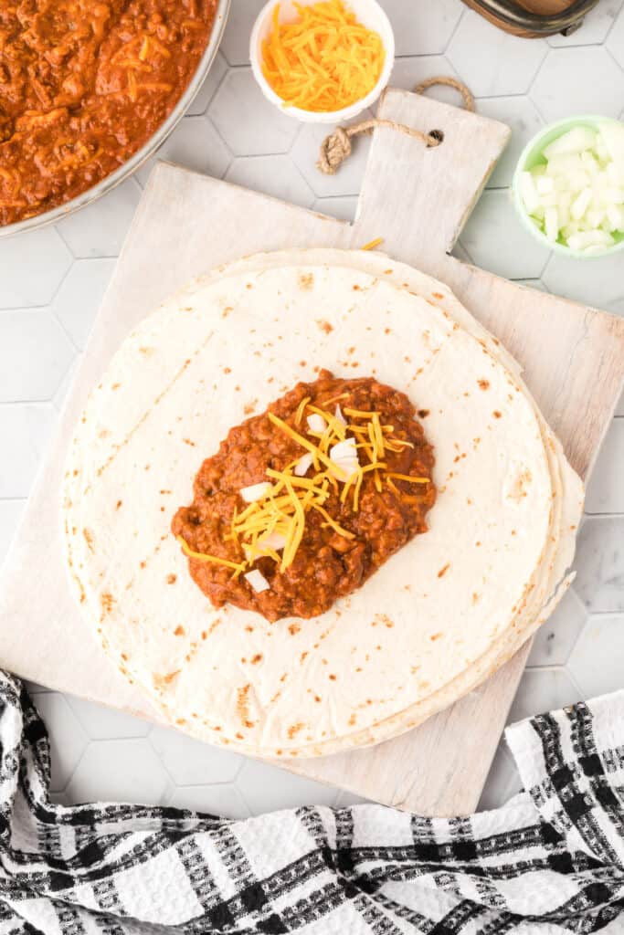 Chili Cheese Burrito filling topped with diced onion and shredded cheddar cheese on a flour tortilla.