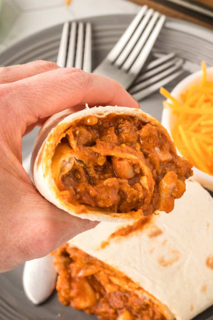 Hand holding a Chili Cheese Burrito with the beefy cheese-filled center visible.