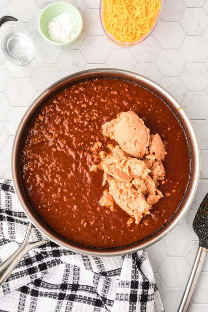 Refried beans added to the simmering chili mixture in a large skillet.
